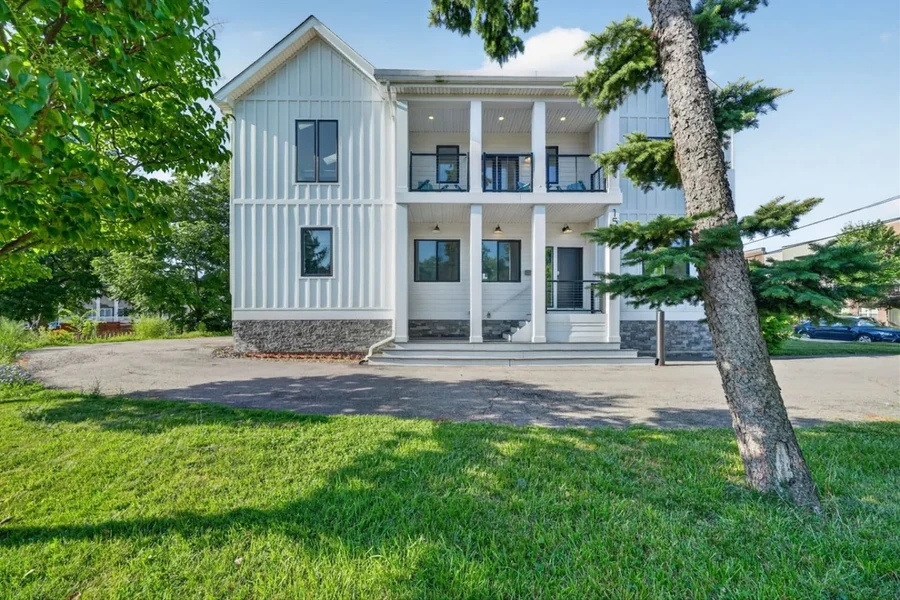 Two-story house exterior with a porch, lawn and trees